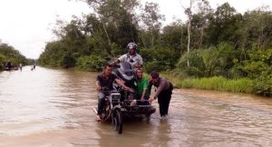 Petugas kepolisian membantu warga yang melintasi genangan banjir di lintasan Meulaboh - Kuala Bhee, di kawasan Ateung Teupat, Kecamatan Bubon, Aceh Barat, Jumat (24/8/2018). (Foto/Dedi Iskandar).