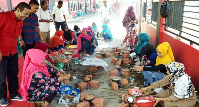 kenduri apam Sekretaris DPW Partai Aceh, Kabupaten Pidie Tgk.Anwar Husen, (baju merah-red) sedang melihat para kaum ibu memasak apam di halaman belakang kantor DPW PA, Pidie. Kamis (12/4/2018). (Foto/Muhammad Riza)