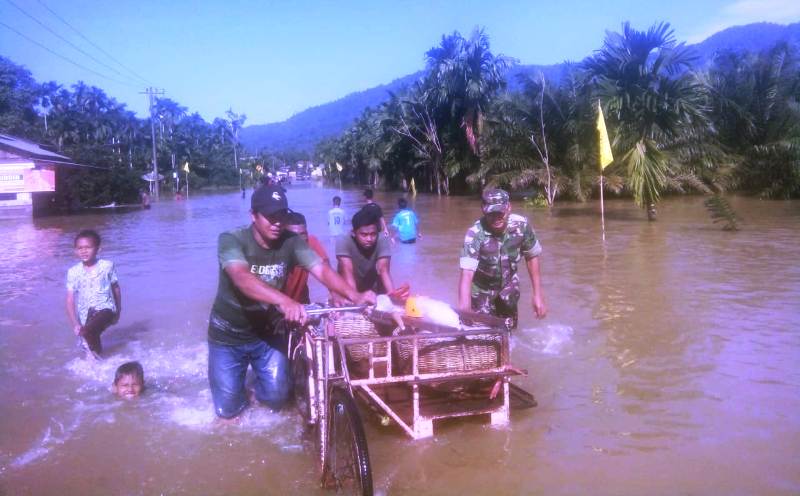 Petugas terlihat membantu warga melintasi jalan yang direndam banjir di Aceh Selatan. (Foto/Ist)